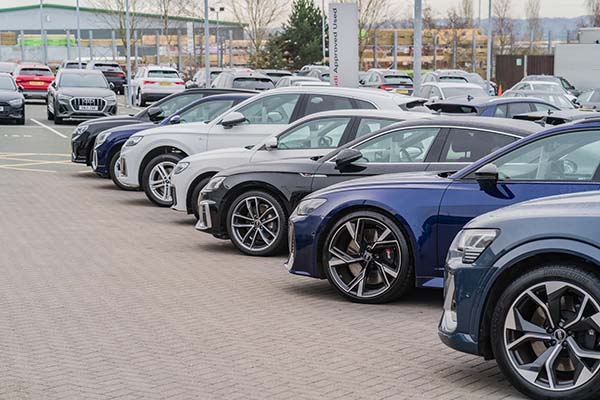 A side-angle view of a row of parked luxury cars, with a blue sedan in the foreground.