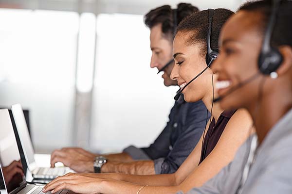 A diverse group of call center agents, wearing headsets, are seated at desks and working on computers.