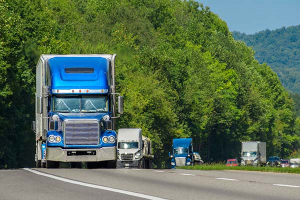 A fleet of semi-trucks on a multi-lane highway, with one large blue truck in the foreground.