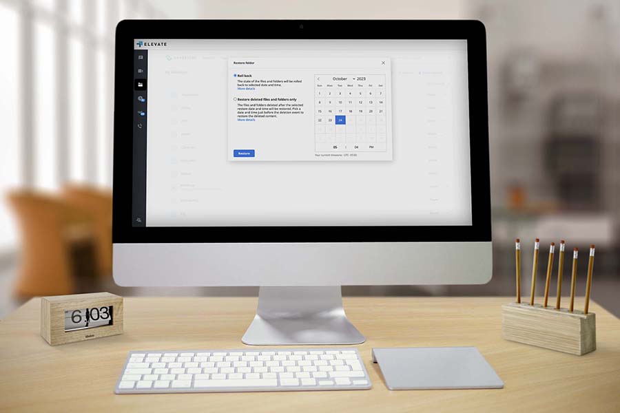A product screenshot for Elevate Technology, showing a monitor on a desk displaying a data backup and restore interface.