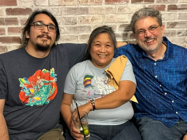 Three colleagues smiling and posing together in front of a brick wall, showcasing the professional team behind Elevate Technology, a mobile technology solution provider.