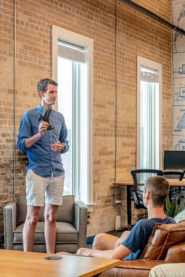  A male professional standing and holding a trophy-like object while speaking to another person in an office setting. This highlights professional development, team collaboration, and IT consulting.