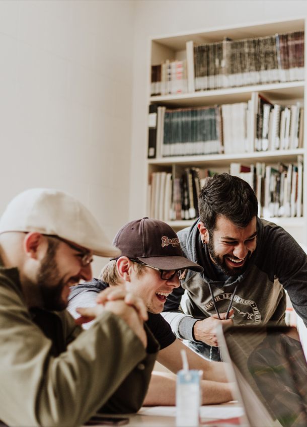 A group of professionals collaborating and laughing while working on a laptop, highlighting team collaboration, IT consulting, and innovative solutions.