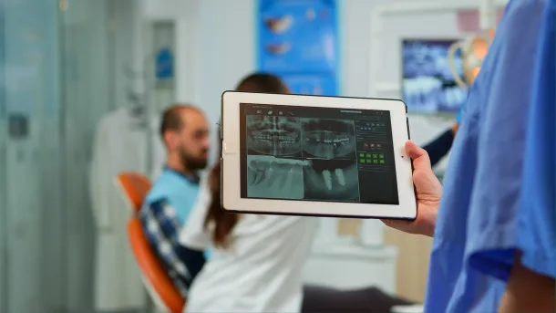 Dental professional holding a tablet displaying a panoramic dental X-ray, showcasing Elevate Technology for smarter communication in a dental practice setting.
