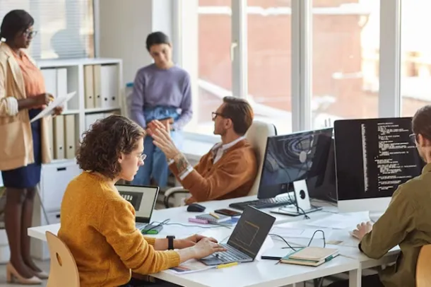 Team of IT professionals collaborating in a modern office using laptops and desktop screens, showcasing teamwork and managed IT solutions, including cloud hosting, business email, and cloud email by Elevation Technology.