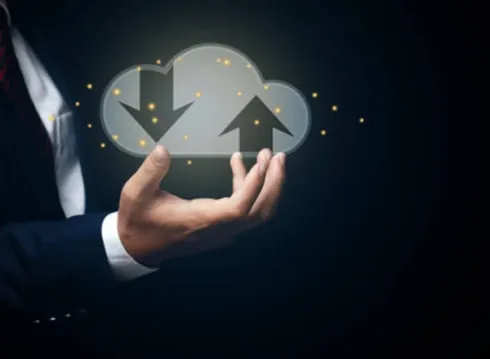 A person's hand holding a glowing cloud icon with upload and download arrows.